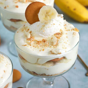 Banana Pudding with whipped cream, a banana slice and cookie on top on a blue background.