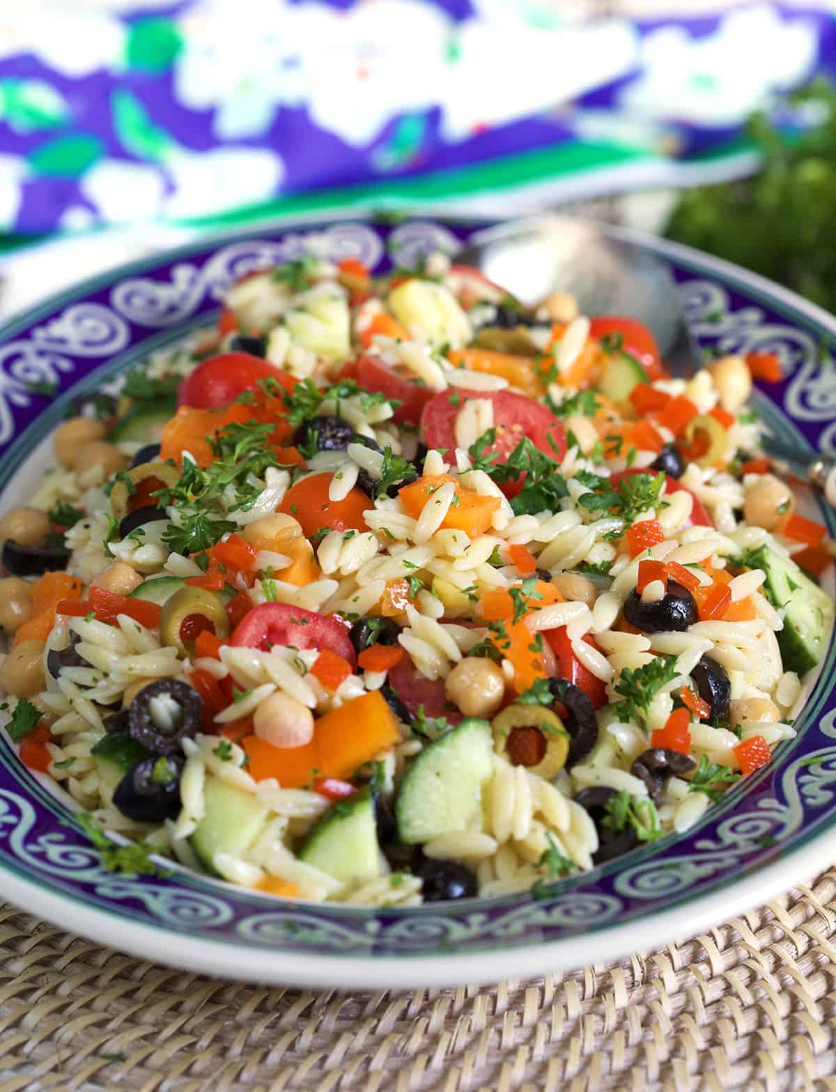 A helping of orzo salad is presented in a blue and white bowl. 