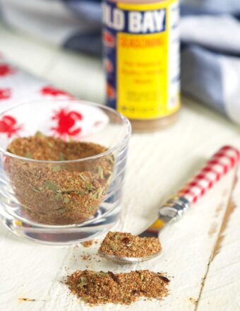 A spoon and small glass container are filled with portions of old bay seasoning.