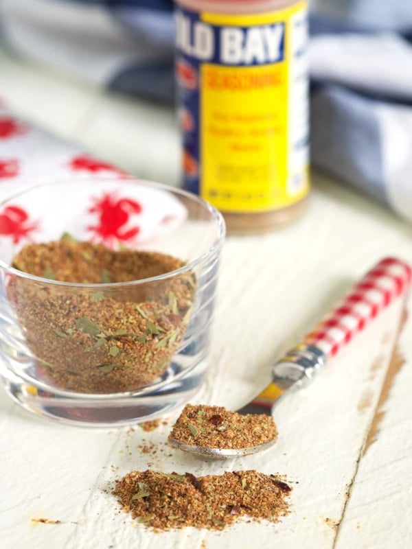 A spoon and small glass container are filled with portions of old bay seasoning.