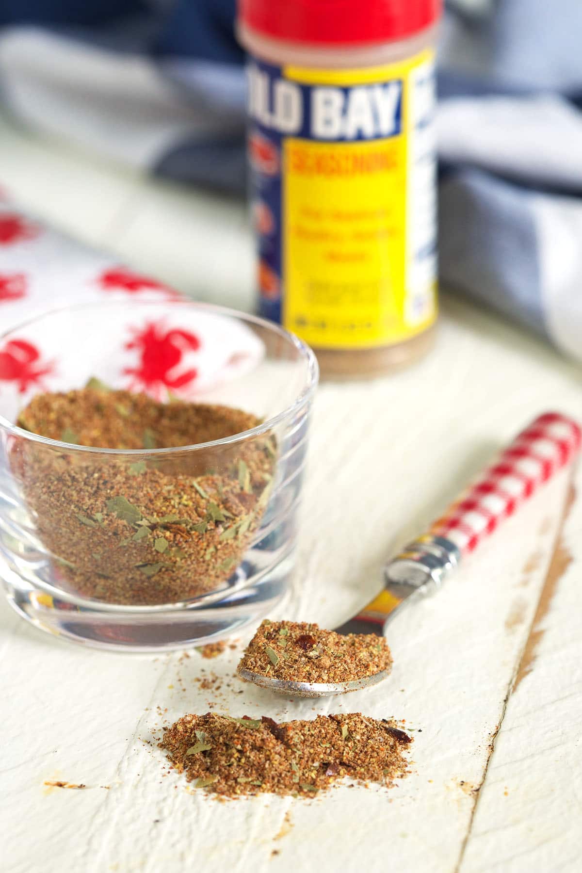 A spoon and small glass container are filled with portions of old bay seasoning. 
