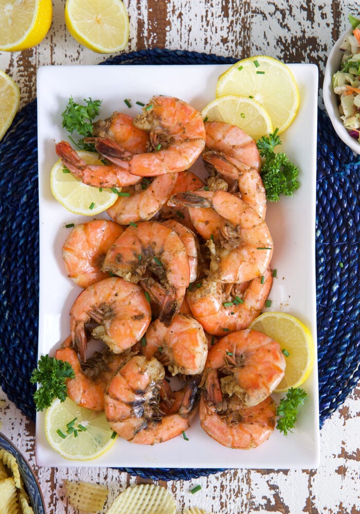 A white plate of steamed shrimp is presented with lemon slices and herbs. 