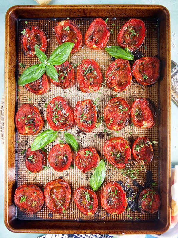 Oven roasted tomatoes on a baking sheet with basil and herbs.
