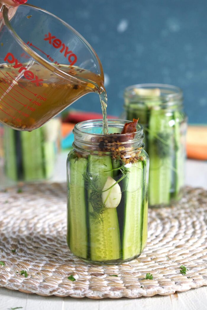 Brine is being poured over sliced cucumbers in a glass jar.