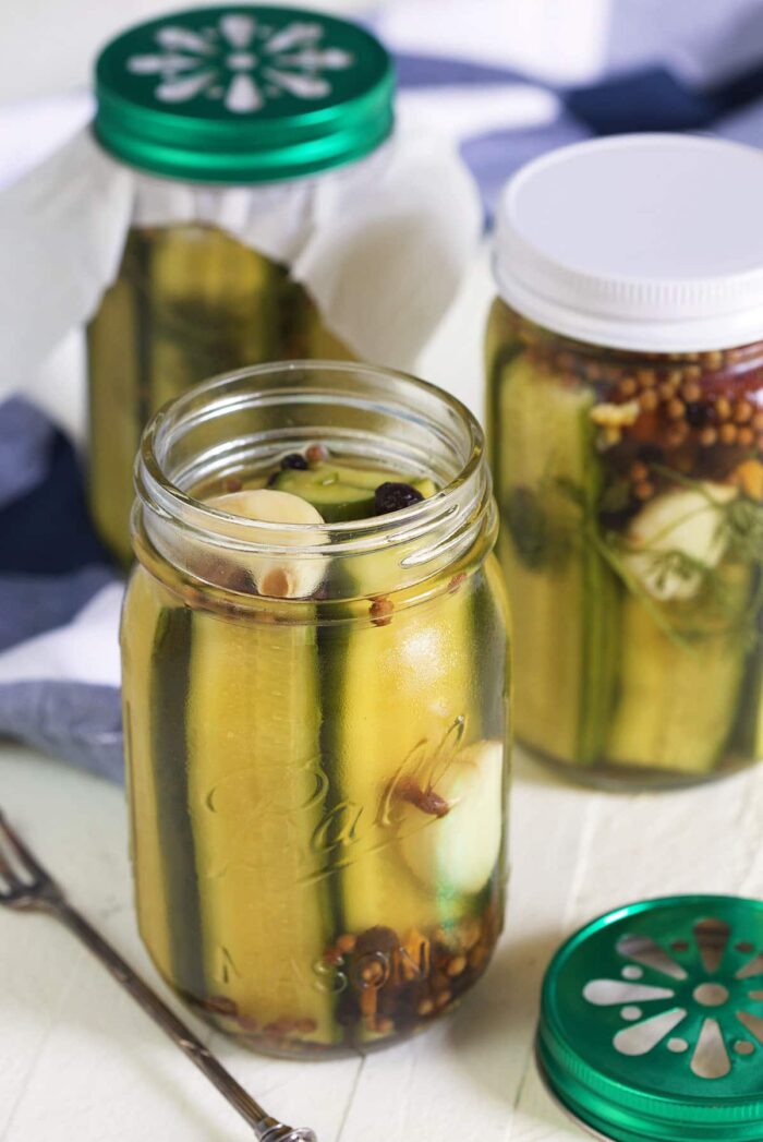 Three jars of pickles are placed on a white surface. 