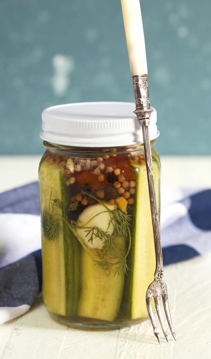 A long fork is placed next to a jar of pickles. 