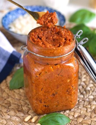 A small spoon is lifting a portion of pesto from the jar.