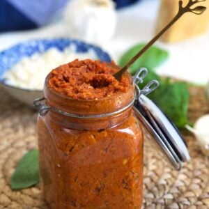 A long spoon is placed in a full jar of tomato pesto.