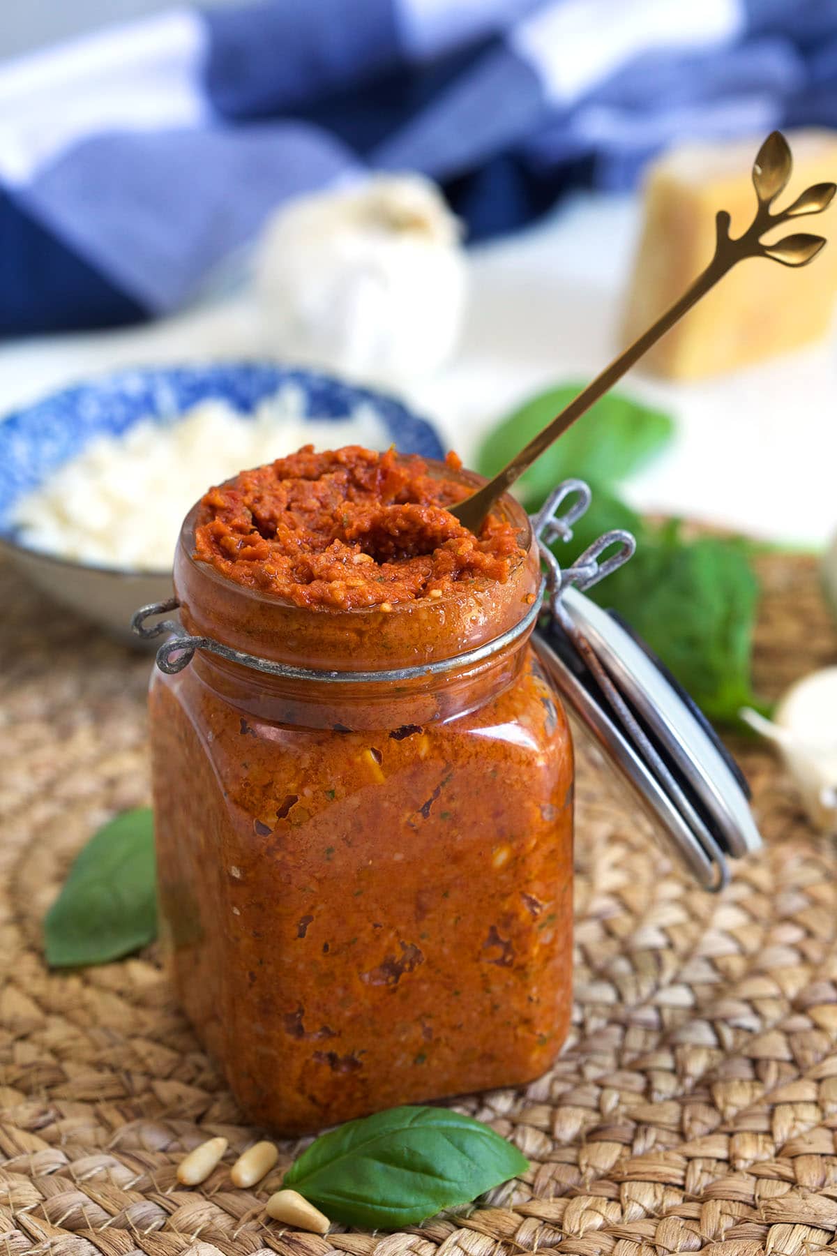 A long spoon is placed in a full jar of tomato pesto.