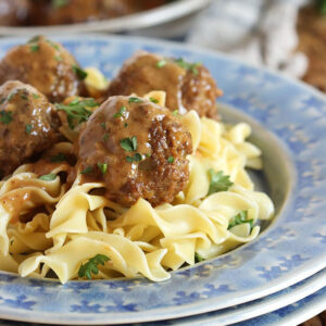 Swedish Meatballs on egg noodles plated on a blue plate set upon a wicker placemat
