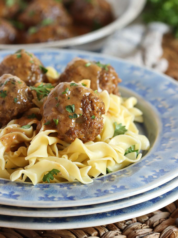 Swedish Meatballs on egg noodles plated on a blue plate set upon a wicker placemat