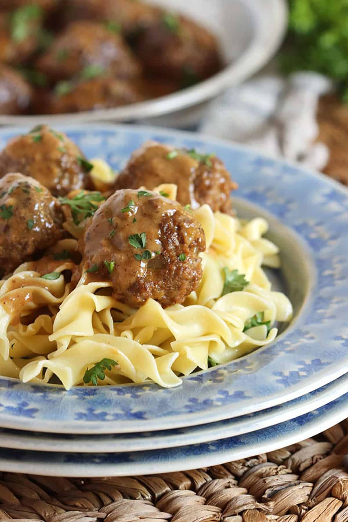Swedish Meatballs on egg noodles plated on a blue plate set upon a wicker placemat