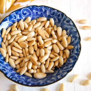 A blue and white bowl is filled with toasted pine nuts.