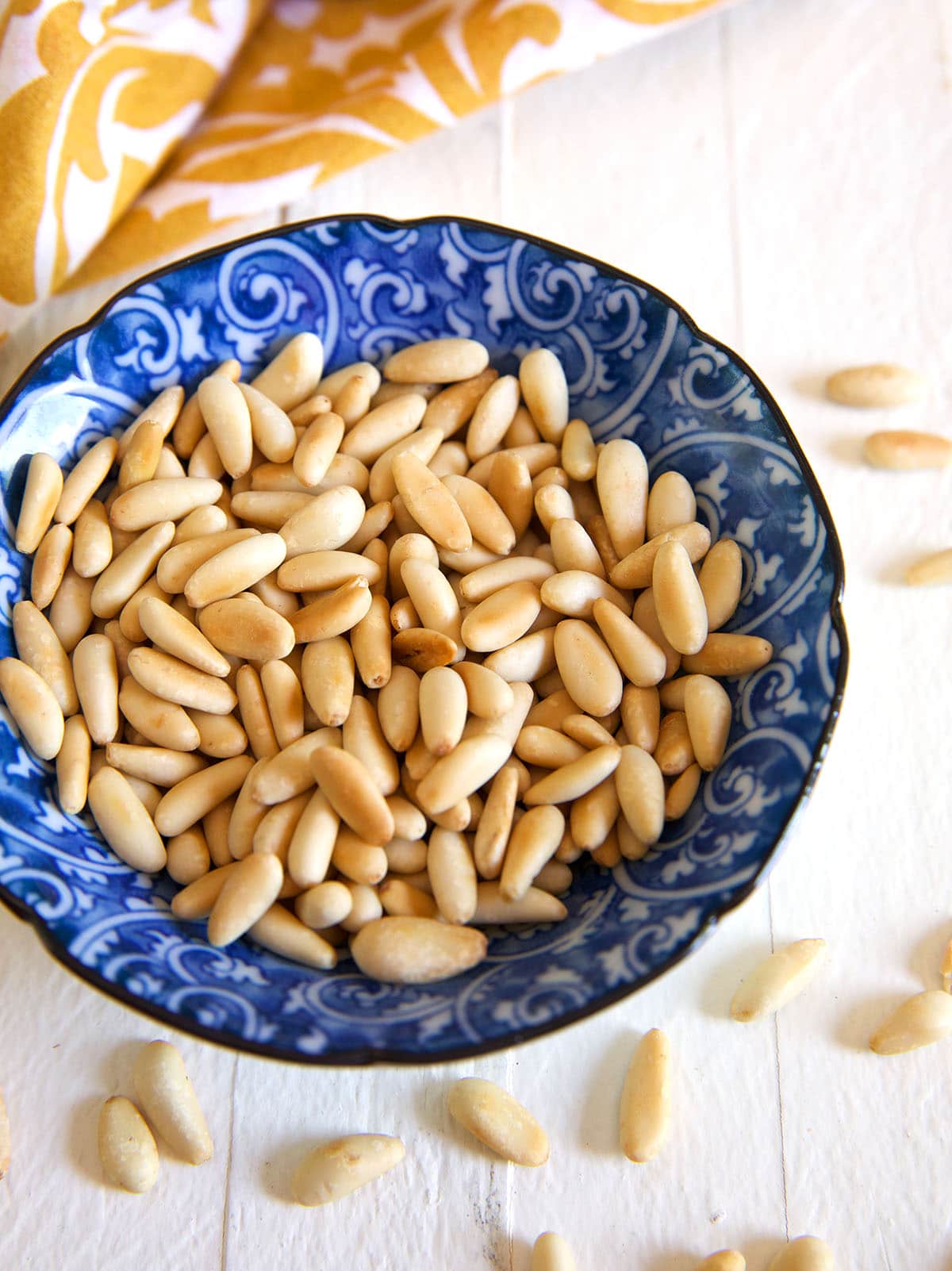 A blue and white bowl is filled with toasted pine nuts. 