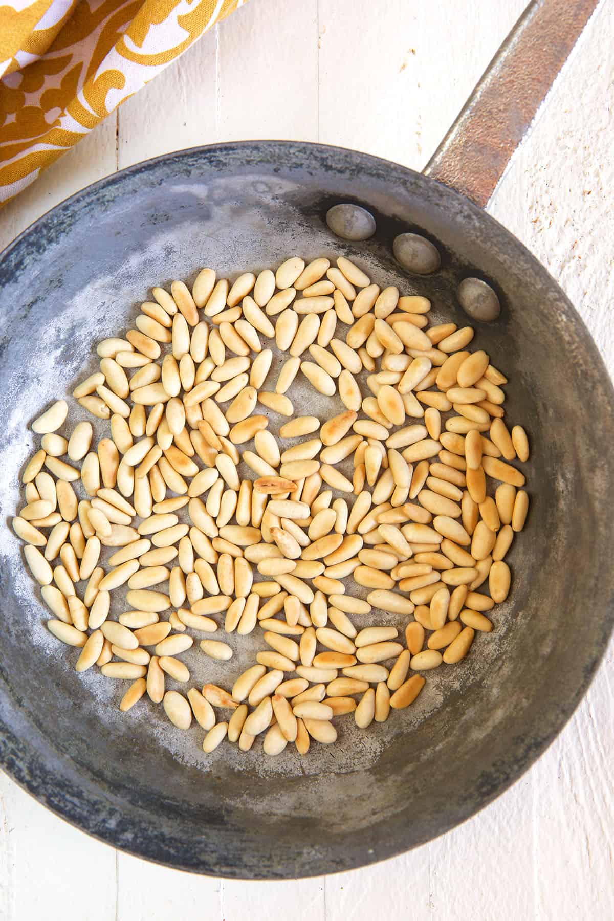 Pine nuts are being toasted in a pan. 