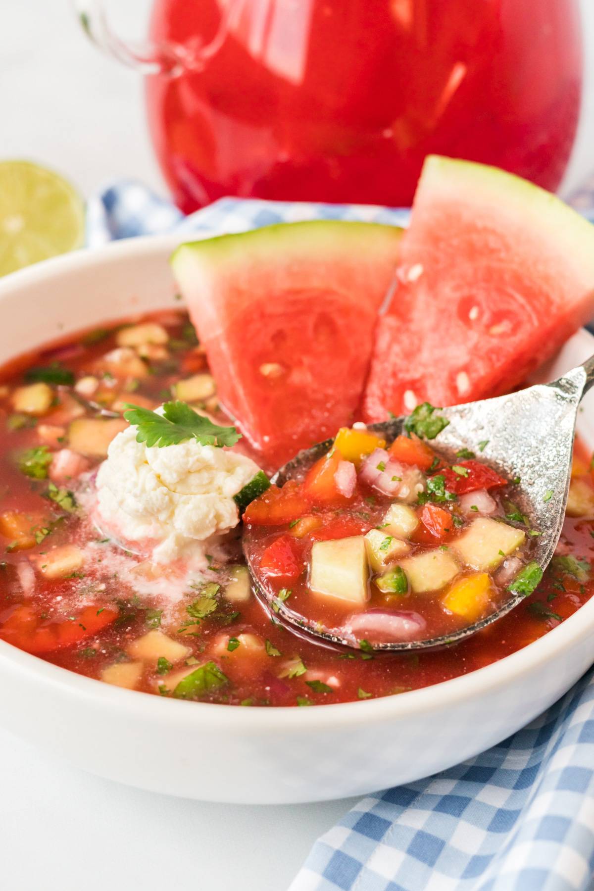 Watermelon gazpacho in a white bowl with a silver spoon and two watermelon wedges.