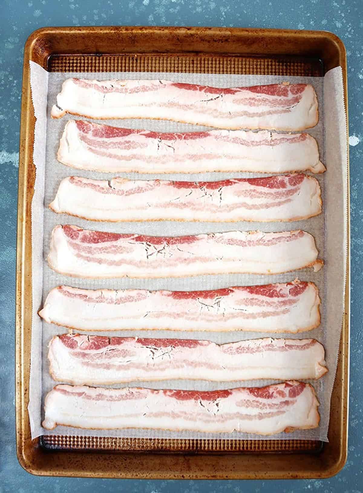 Overhead shot of raw bacon on a baking sheet.