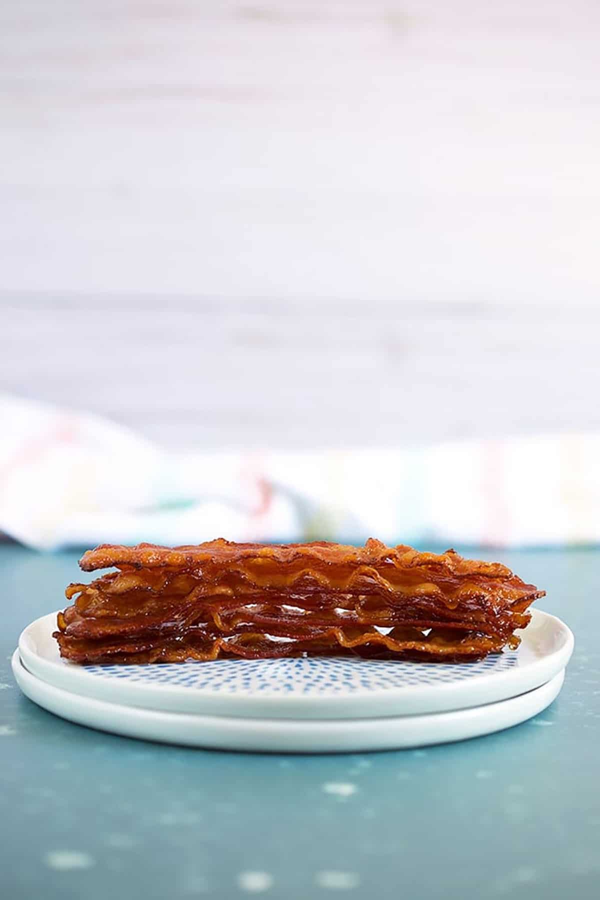 8 stacked bacon slices on a white plate on a blue background.