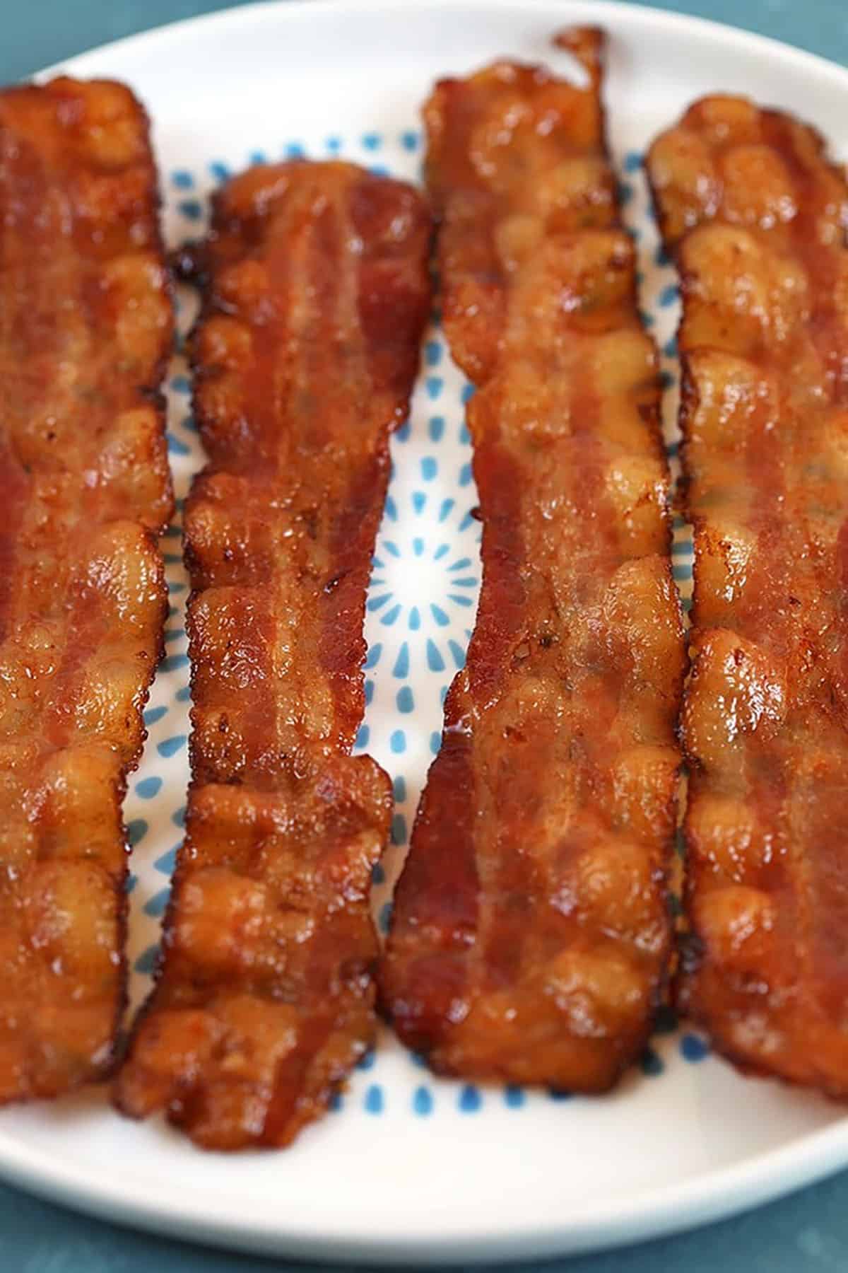 Four sliced of bacon on a white plate with blue dots.