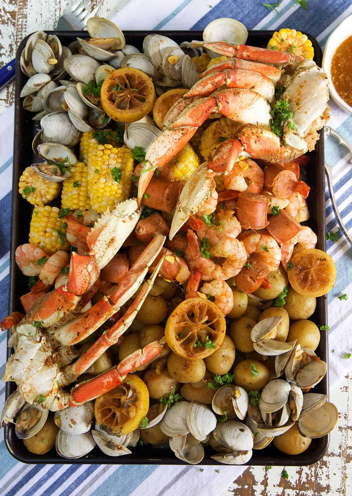 Crab legs, shrimp, clams, corn and potatoes are all boiled and placed on a serving platter.