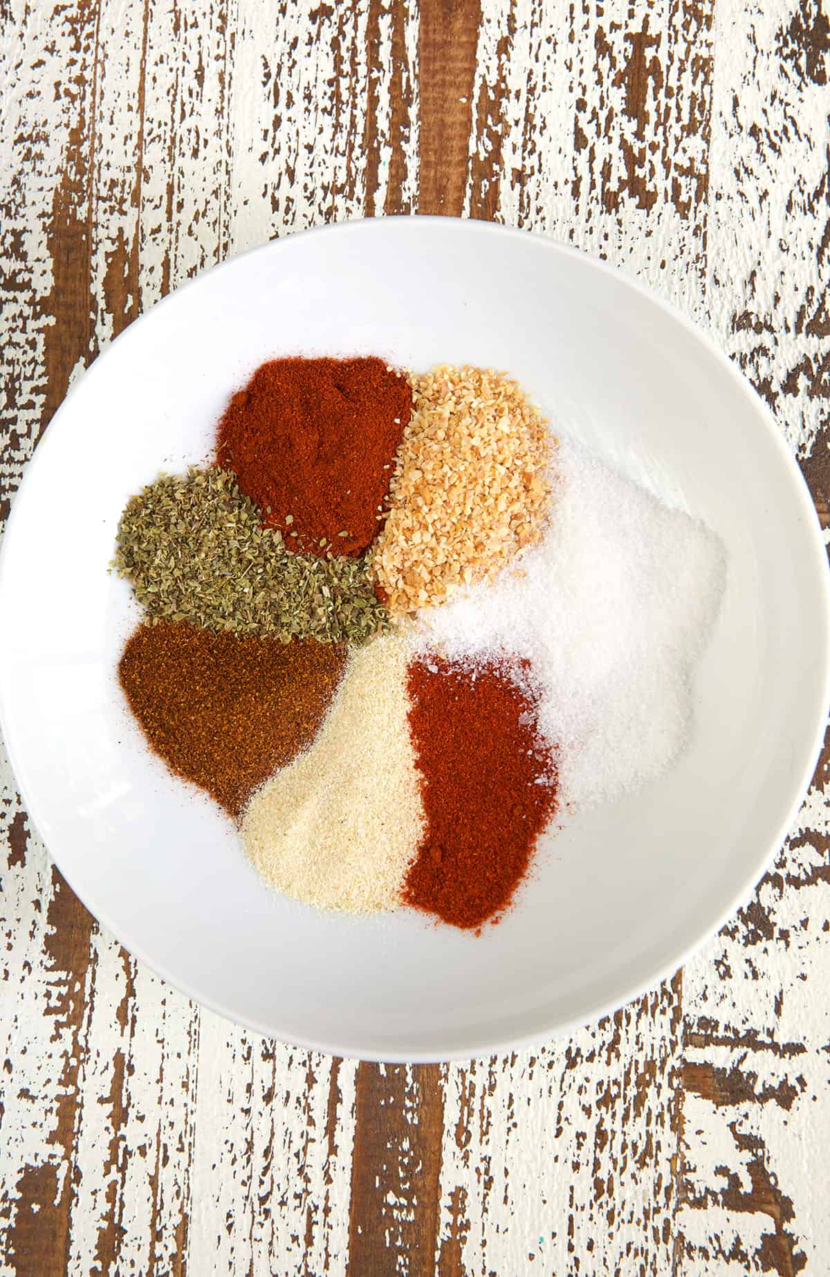 A white bowl has an unmixed presence of seasonings. 