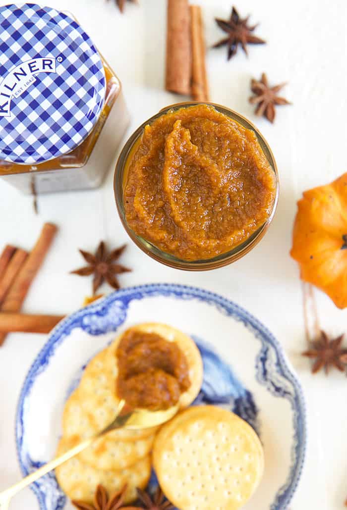 A jar of pumpkin butter is placed next to crackers and loose spices. 