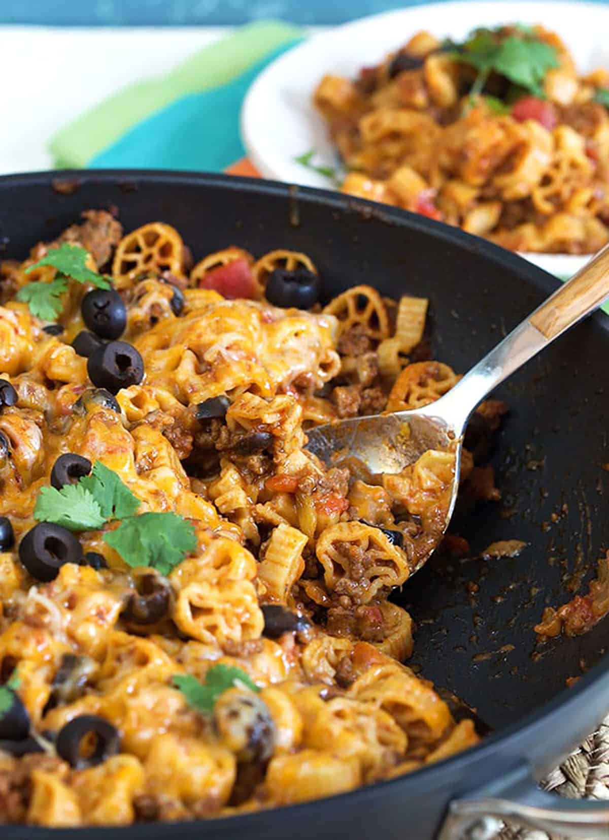 close up of taco pasta in a black skillet with a wooden spoon.