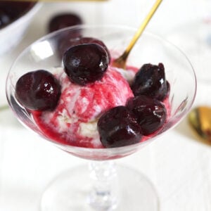 Cherries and red syrup cover a scoop of vanilla ice cream in a martini glass.