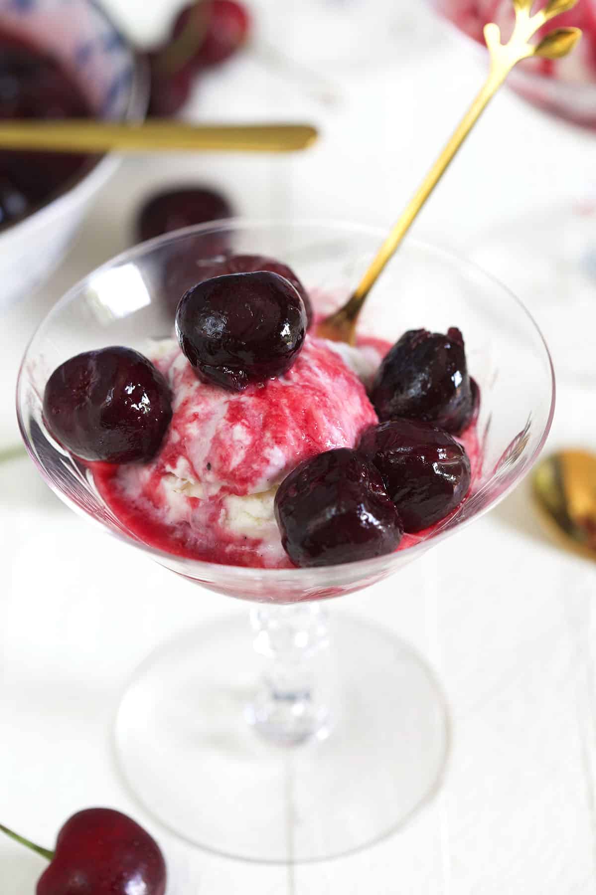 Cherries and red syrup cover a scoop of vanilla ice cream in a martini glass. 