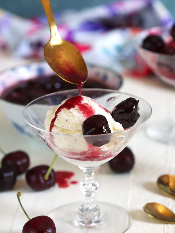 A spoon is drizzling syrup onto a serving of vanilla ice cream.