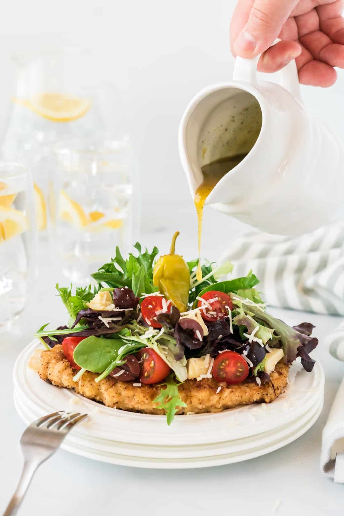 dressing being poured over Chicken Milanese on a white plate.