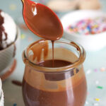 Homemade Magic Shell in a glass jar with a pink spoon drizzling the sauce.