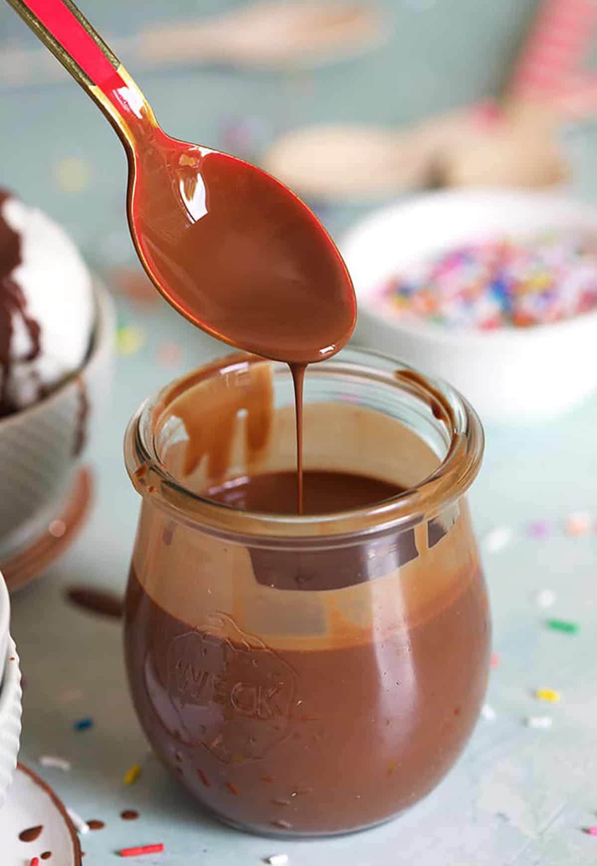 Homemade Magic Shell in a glass jar with a pink spoon drizzling the sauce.