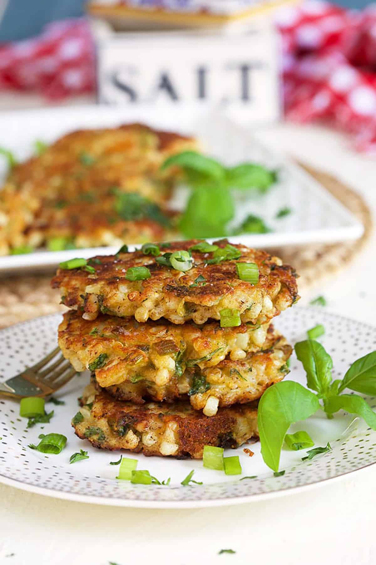 stacked corn fritters on a white plate with basil and a salt box in the background.