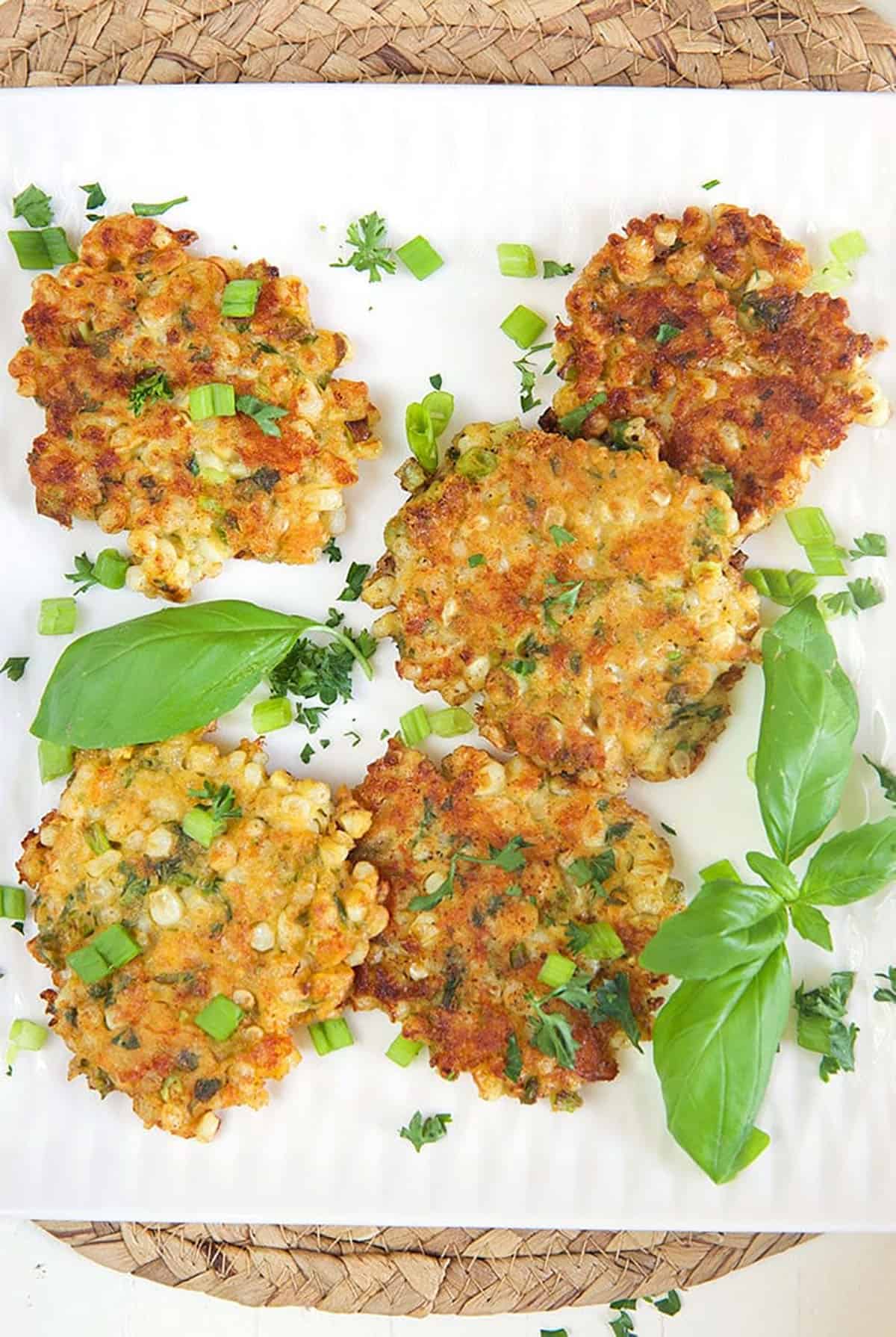 Overhead shot of corn fritters on a white platter with basil.