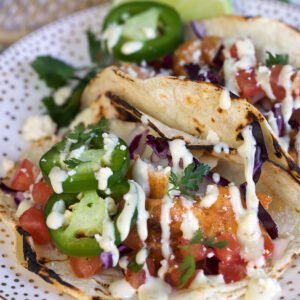 Jalapeno slices and lime wedges are placed on a plate with fish tacos.