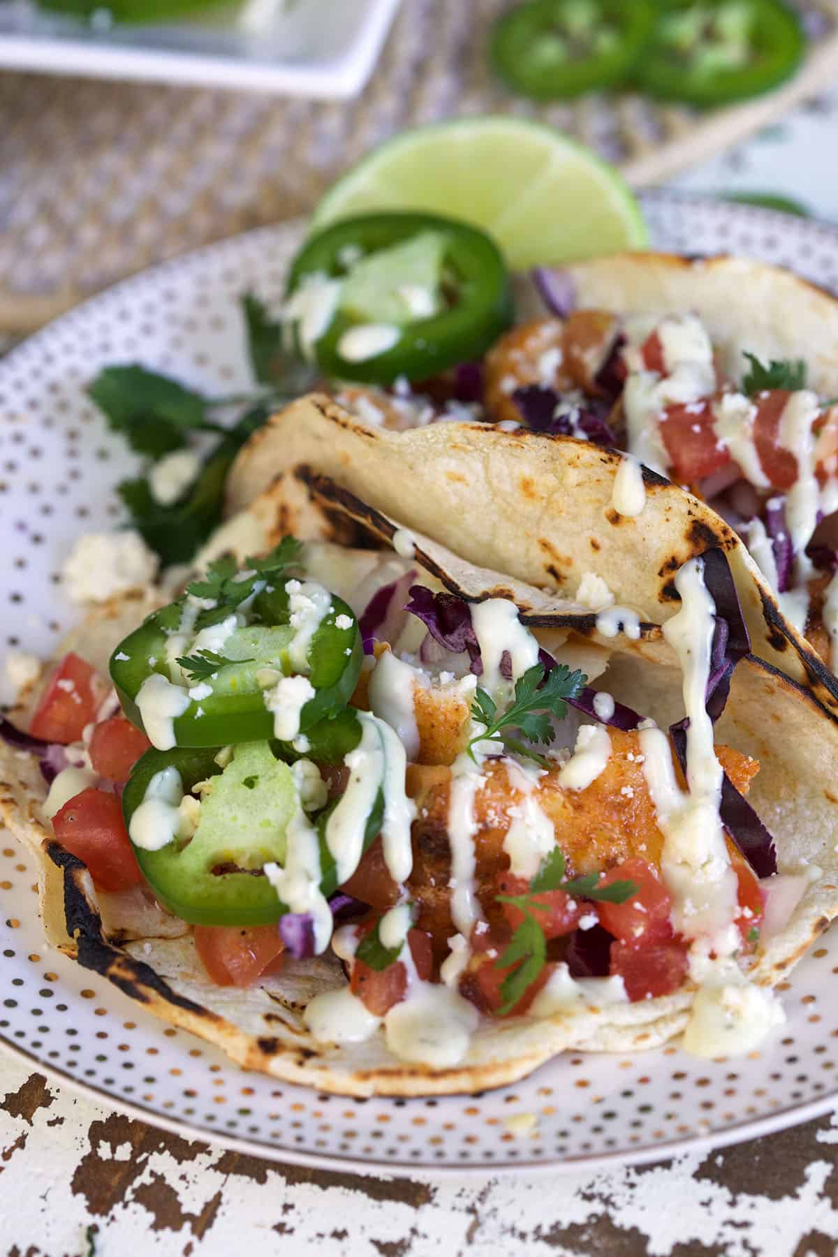 Jalapeno slices and lime wedges are placed on a plate with fish tacos. 