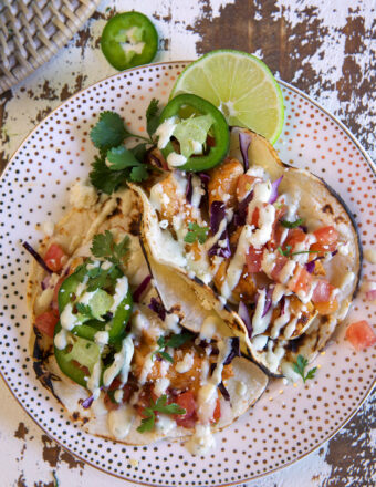Several cod tacos are on a spotted plate.