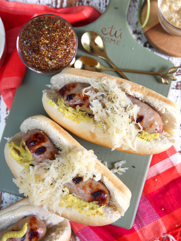 Two beer brats are placed on a surface with other ingredients and spoons.