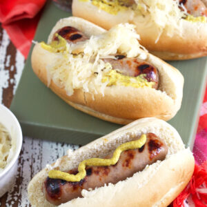 Three beer brats are topped with mustard and sauerkraut.