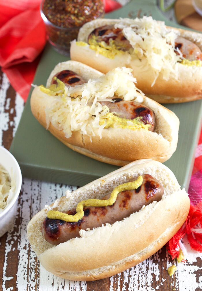 Three beer brats are topped with mustard and sauerkraut. 