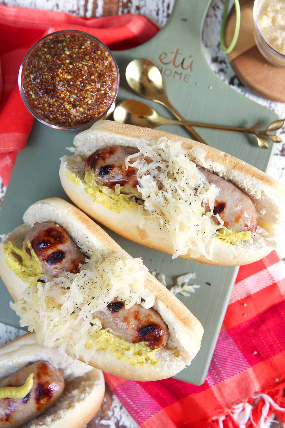 Three beer brats are placed on a green wooden cutting board. 