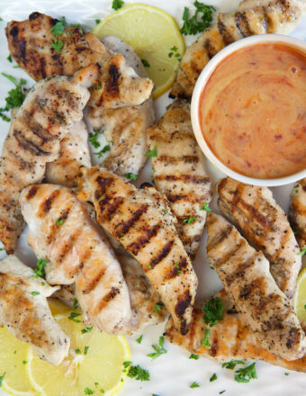 Grilled chicken tenders are placed around a bowl filled with spicy honey mustard.
