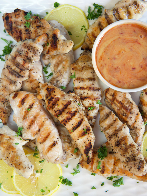 Grilled chicken tenders are placed around a bowl filled with spicy honey mustard.