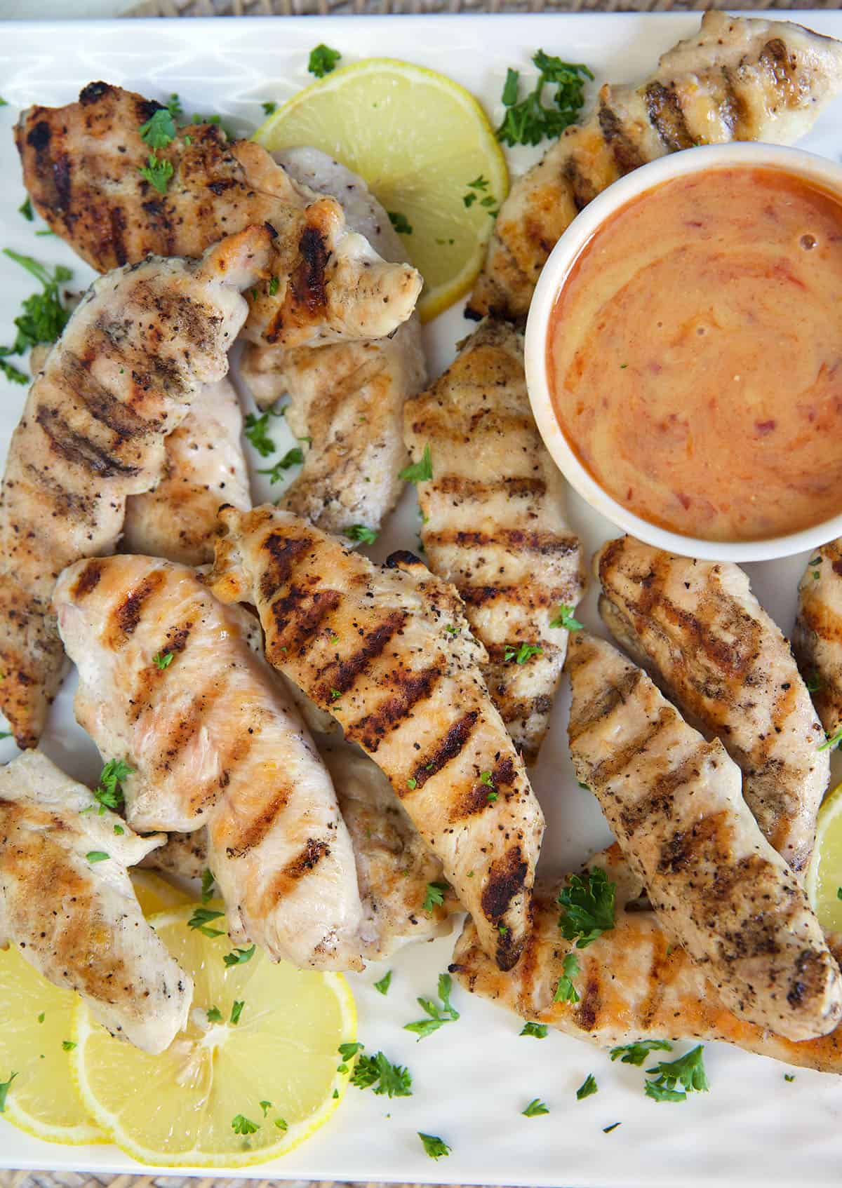 Grilled chicken tenders are placed around a bowl filled with spicy honey mustard. 