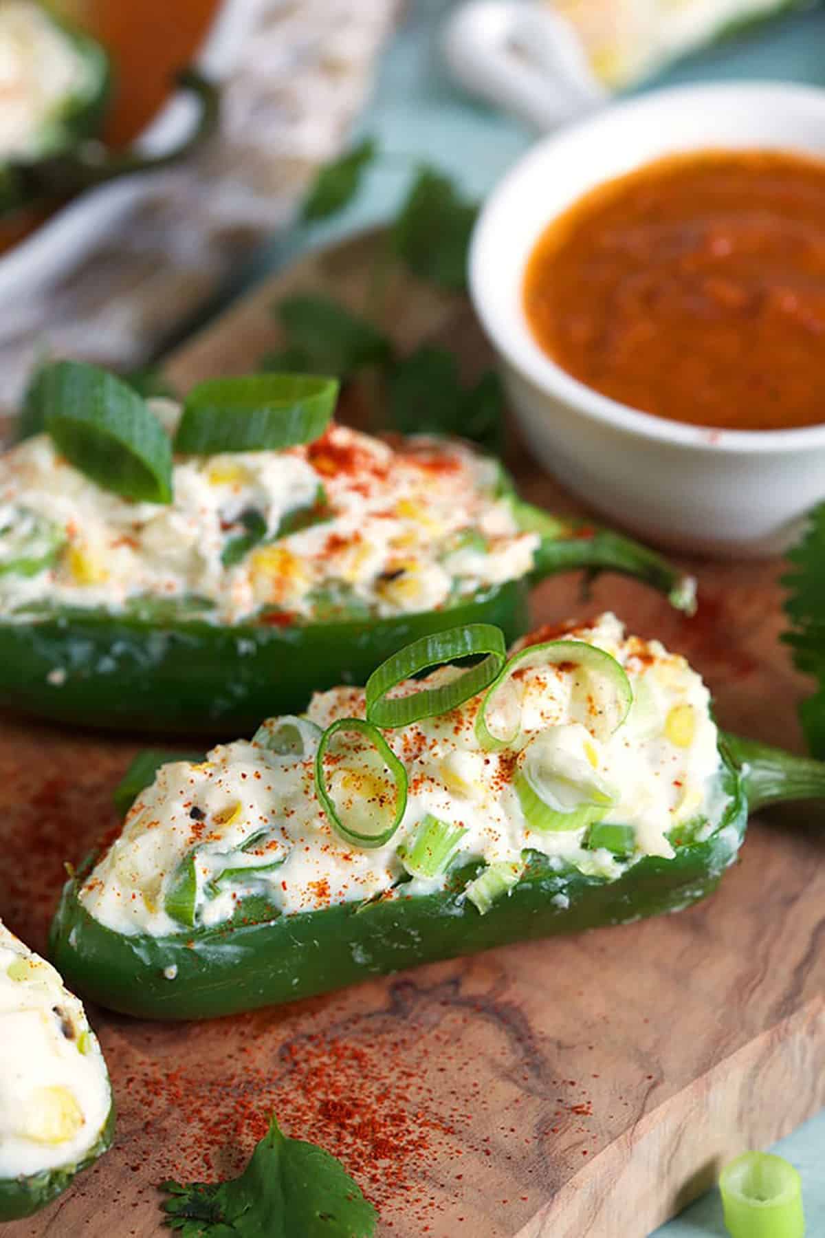 Grilled jalapeno poppers on a plate with red pepper sauce.