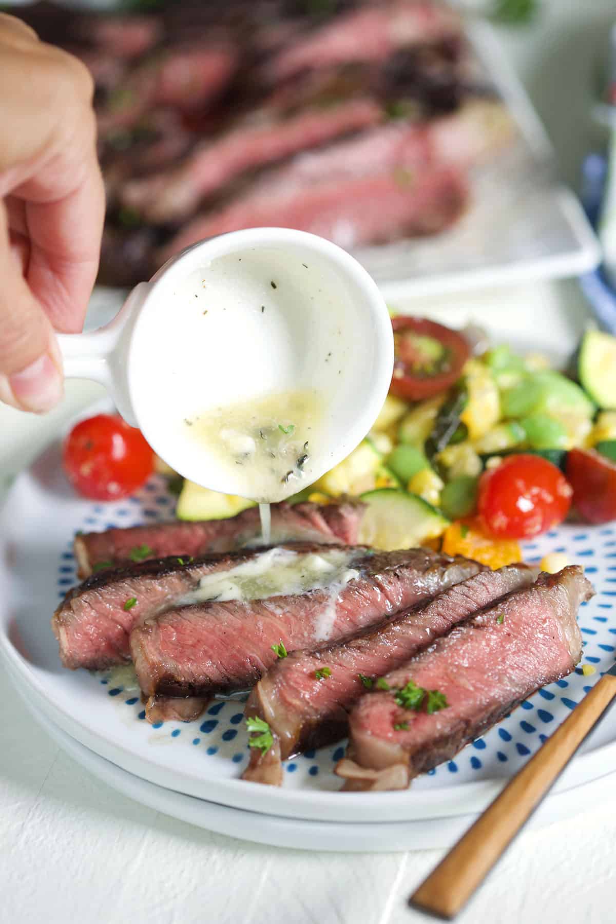 Garlic butter sauce is being drizzled over sliced steak. 