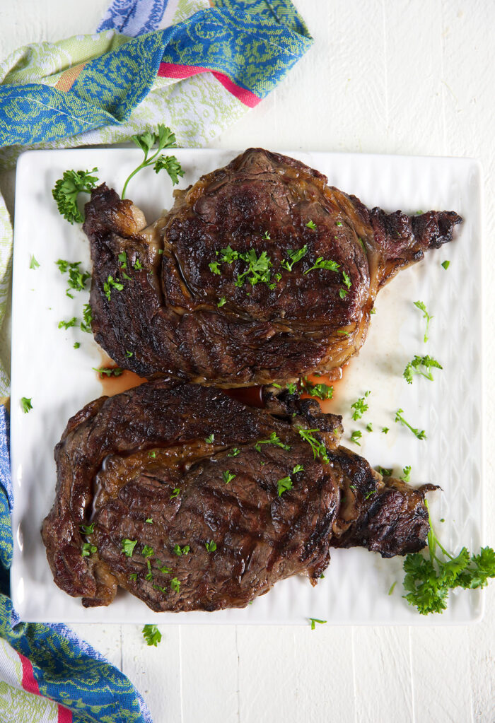 Two grilled ribeyes are placed on a white plate. 