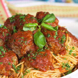 Italian Meatballs on a pile of spaghetti with tomato sauce in a white bowl.