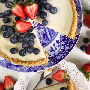 No Bake Cheesecake with blueberries and strawberries on top served on a blue and white cake plate.